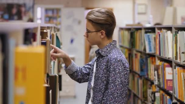 A young guy in glasses chooses a book in a library — Stock Video