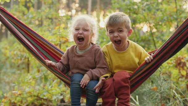 Двоє дітей голосно кричать, сидячи в гамаку — стокове відео
