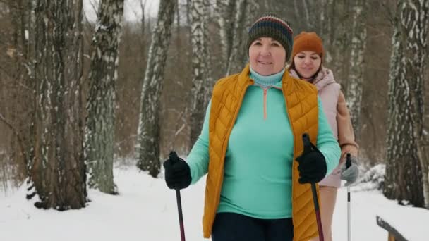 Een oudere vrouw met haar dochter van middelbare leeftijd zijn bezig met nordic walking in de winter — Stockvideo