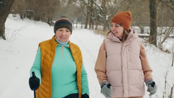 Mujer anciana feliz con hija práctica Nordic caminar en invierno en la naturaleza — Vídeos de Stock