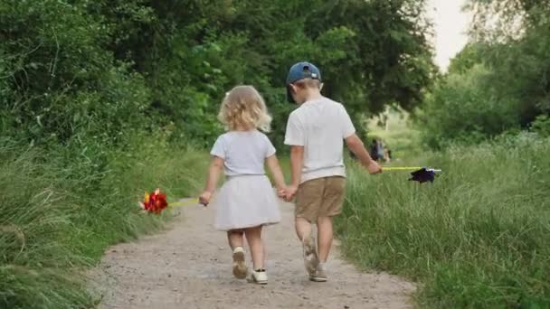 Vista posterior niño y niña tomados de la mano están caminando al aire libre — Vídeo de stock