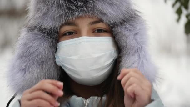 Porträt eines Teenagers mit Pelzmütze, der ihr eine medizinische Maske vom Gesicht nimmt — Stockvideo