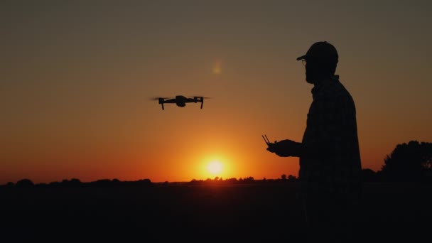 Silhueta de um homem controla um drone ao pôr-do-sol — Vídeo de Stock