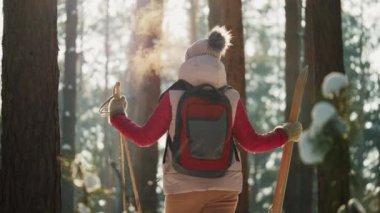 Kayak ve sırt çantalı bir kadın kış ormanına bakıyor.