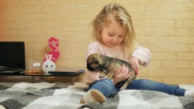 Küçük kız yatakta otururken köpeğini nazikçe okşuyor.