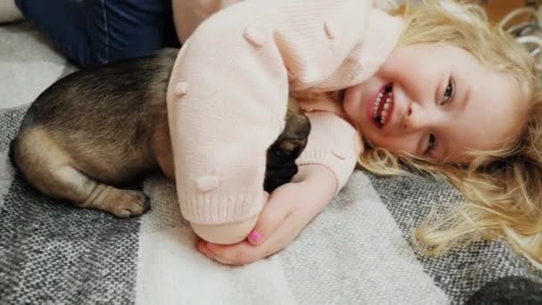 Маленька дівчинка грає зі своїм щеням, що лежить на ліжку — стокове відео
