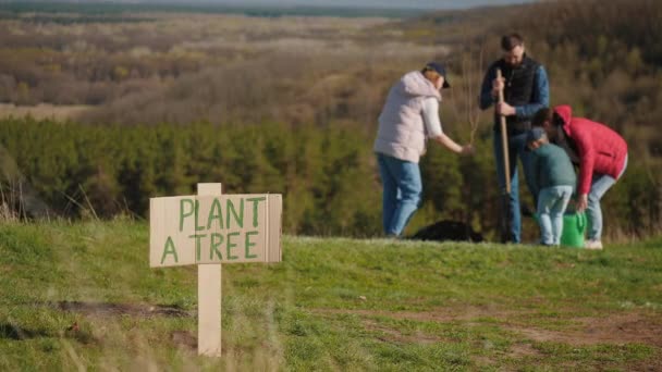 Un signo con la inscripción Planta un árbol en el fondo de una familia de plantar un árbol — Vídeos de Stock