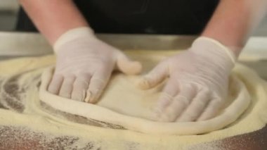 Şef pizza için hamur yapıyor ve elleriyle yoğuruyor.