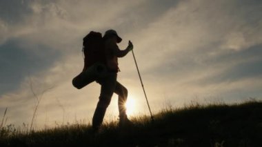 Sırt çantalı, dağda yürüyen kadın silueti.