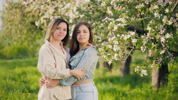 Портрет женщины с дочерью-подростком, стоящей в цветущем саду — стоковое видео