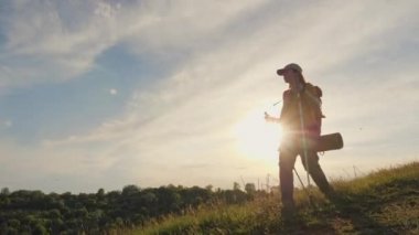 Yürüyüş direkleri olan bir kadın gün batımında dağlarda seyahat eder.