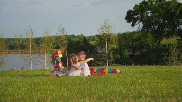 Niño y niña se abrazan mientras están sentados en la hierba en el parque — Vídeos de Stock