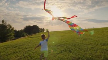 Küçük çocuk gün batımında çayırda uçurtmayla oynuyor.