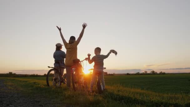 Family with bicycles standing at sunset and waving with hands — Stok Video