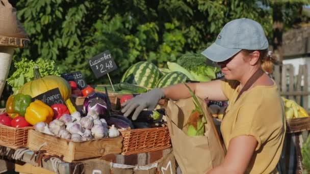 A nő a piacon papírzacskóba teszi a zöldségeket. — Stock videók