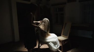 Terk edilmiş bir evin eski ve korkunç odasında bir kızın saçını tarayan bir kadın.