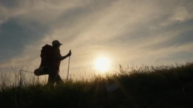 Sırt çantalı bir kadın gün batımında dağa tırmanıyor.