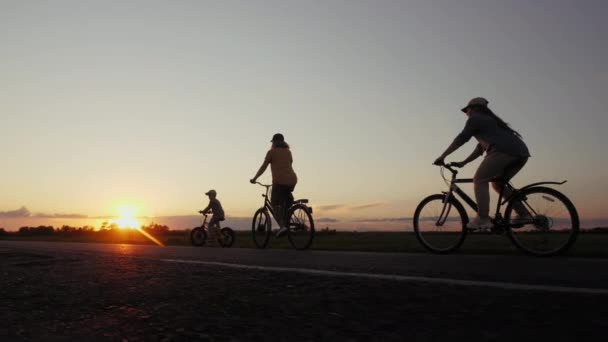 Çocuklu anne siluetleri gün batımında bisiklet sürüyor. — Stok video