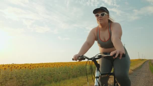 Mulher com excesso de peso no sportswear monta uma bicicleta em uma estrada de terra — Vídeo de Stock