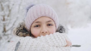 Açık havada örülmüş şapkası ve atkısı olan sevimli bir kızın portresi.