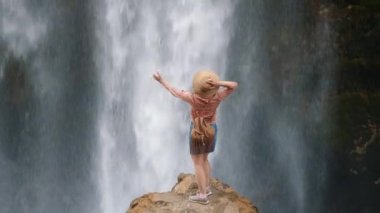 Bir kadın taşın kenarında dururken şelalenin tadını çıkarıyor.