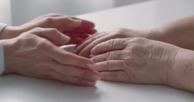Video, genç bir bayanın yaşlı ellerini tutup onları sakinleştirici ve destekleyici bir jest olarak bir arada tuttuğunu gösteriyor.
