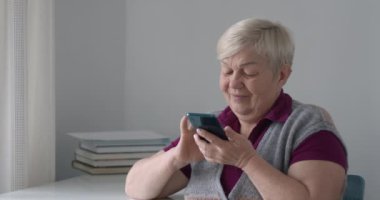 Yaşlı bir kadın akıllı telefon kullanır. Yaşlı kadın evde otururken cep telefonuna bir mesaj yazıyor..