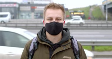 Şehrin caddesinde koruyucu maskeli bir adamın portresi. Geçen arabaların arka planında maskeli genç bir adam var..