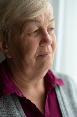 Pencereden dışarı bakan yaşlı bir kadının yüzü. Yaşlı üzgün kadının yakın plan portresi..