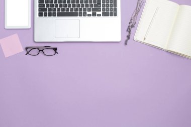 Dizüstü bilgisayarı ve modern ofis özellikleri olan şık, kadınsı bir iş masası. Üst Manzara. Uzayı kopyala Düz alan. Mor arkaplan.
