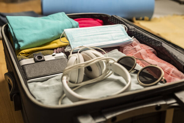 Women's hands are packing a suitcase with things for travel, along with protective masks.