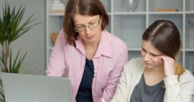 Anne ve kızı evdeki dizüstü bilgisayara uzaktan bakarak ders alıyorlar. Ev ödevi yapan kadın öğretmen. Eğitim kavramı.