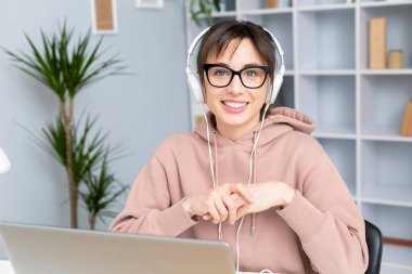 Gözlüklü ve kulaklıklı bir kadın dizüstü bilgisayarda çalışıyor. 