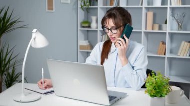 Dizüstü bilgisayarda çalışan ve telefonda konuşan güzel bir genç kadının portresi..