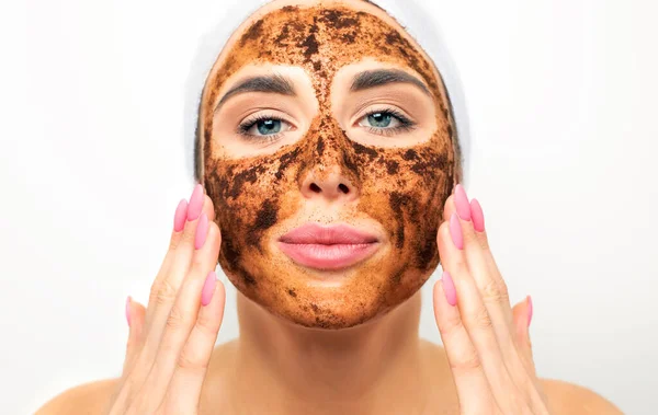 Facial skin scrub. Coffee grounds mask on the face of a beautiful young woman. Organic natural cosmetology.