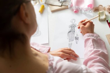 Tasarımcı, işyerindeki kağıt üzerine şık kadın kıyafetleri çiziyor..