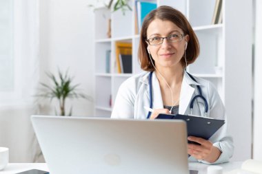 Terapist doktor panoya yazı yazıyor ve kulaklıkları dinlerken kameraya bakıyor.