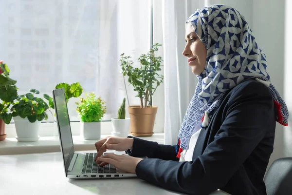 Wanita Muslim Dalam Hijab Menggunakan Laptop Oleh Jendela Dengan Tanaman — Stok Foto