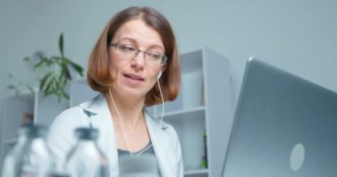 Dost canlısı kadın terapist portresi. Bilgisayarlı web kamerası kullanarak hasta video iletişimine danışmanlık yapıyor. Kulaklıklı bir kadının uzaktan konuşma görüntüsü..