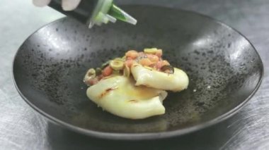 Mutfakta profesyonel bir aşçı soslu kalamar hazırlıyor. Şef tabağı yeşil otlarla süsledi. Lezzetli gurme yemeği ev mutfağında hazırlandı.