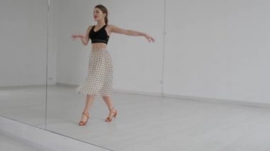 Çekici kız, parlak beyaz bir salonda aynanın önünde dans ediyor. Profesyonel bir balo dansçısı koreografi salonunda antrenman yapar..