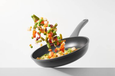 Taze sebzeler beyaz arka planda bir tavada uçar. Tavada çeşitli doğranmış sebzelerle yemek pişirmek. Sağlıklı yeme ve diyet kavramı.