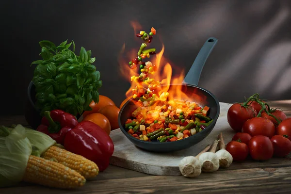 Ateş alevi olan tavada çeşit çeşit kızarmış sebzeler. Tavada uçuşan flambe sebzeleri. Restoran menüsü, yemek pişirme, Asya yemekleri. 