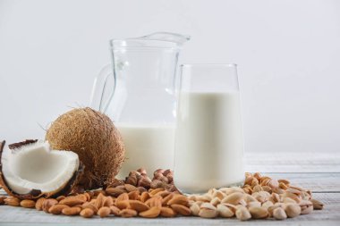 Bardakta sebze sütü ve tahta bir arka planda sürahi. Farklı malzemelerden sebze sütü: Hindistan cevizi, fındık, kaju, fıstık, badem. Sağlıklı Yeme 