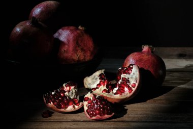 Karanlık, atmosferik, durgun bir hayat. Açık nar ve sulu kırmızı tohumlar, ahşap bir masaya saçılmış, siyah bir arka plana çarpıcı yönlü ışıkla vurgulanmış..