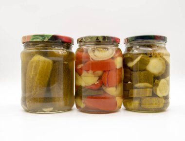 Üç şeffaf kavanoz, turşu, salatalık, domates ve biber, beyaz arka planda..