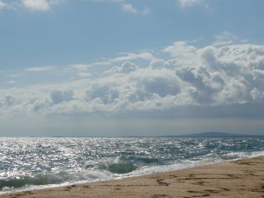 Boş bir kumsal ve bulutlu bir gökyüzünün altında köpüklü bir deniz. Deniz güneşin altında gümüş rengidir..