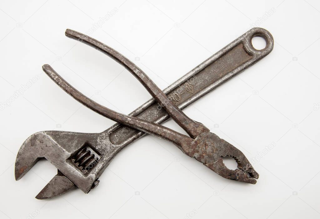 Old rusty pliers and an adjustable wrench on a white background.