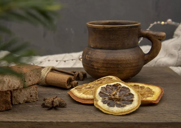 Una taza de cerámica marrón, dulces y especias aromáticas están en una bandeja de madera contra una pared gris. — Foto de Stock