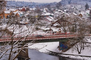Kış kırsal arazisi. Nehir kıyısında karla kaplı bir köy bir yol köprüsü tarafından geçiliyor..